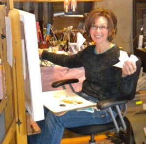 photo of a woman sitting in a chair painting on a canvas