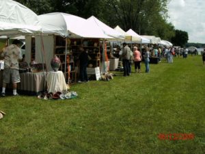 photo of white tents lined up in the grass with vendors selling items out of them