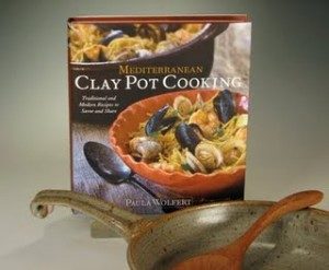 photo of a green clay skillet with a wooden spoon in it next to a cookbook