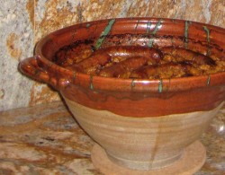 photo of a bright orange cassole with a cassoulet inside