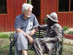 photo of an elderly man sitting on a bench next to a statue of a person sitting on the bench