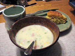 photo of a bowl of potato soup with a spoon in it with a cup and plate next to it