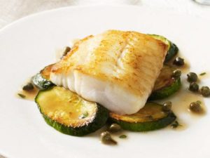 photo of a fish fillet in top of baked zucchini on a white plate