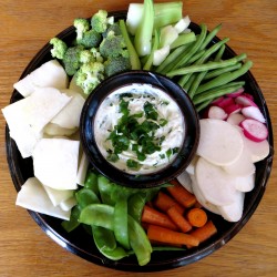 photo of a blue chip and dip bowl with vegetables around it and dip in the middle