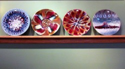photo of 4 colorful ceramic plates facing standing upright on a shelf