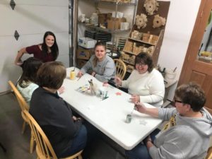 photo of a group of six ladies around a table painting clay ornaments