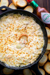 photo of a cheesy shrimp dip in a cast iron skillet with bread pieces and tabasco sauce