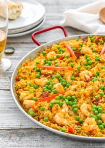 photo of paella with yellow rice, peas, shrimp, and red peppers in a dish