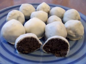 Photo of dark brown oreo truffles covered in white chocolate on a blue striped plate
