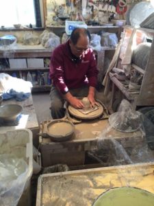 photo of a man sitting at the pottery wheel sculpting a piece