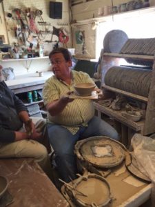 photo of a man sitting at a pottery wheel holding is finished piece in the air on a pottery wheel bat