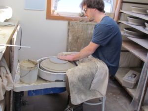photo of a man sitting at a pottery wheel sculpting a large bowl