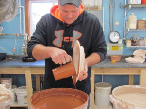 photo of joe nagel pouring glaze on a piece of pottery 