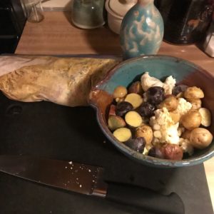 photo of a bowl with vegetables in it next to a wood cutting board with a knife and raw chicken