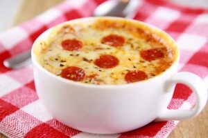 photo of a pepperoni pizza made in a white mug on a red and white checkered tablecloth