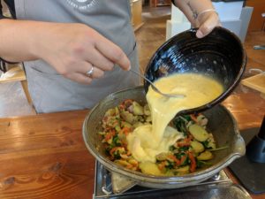 Morgan adding eggs to cooked veggies in a clay coyote flameware skillet.