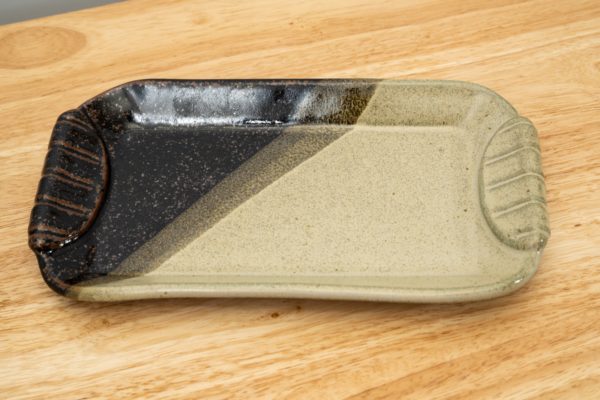 the photograph shows a clay coyote small tray glazed in mint chip resting on a light colored wooden surface. the tray is partially black, and partially mint green. the photograph is lit with white light.