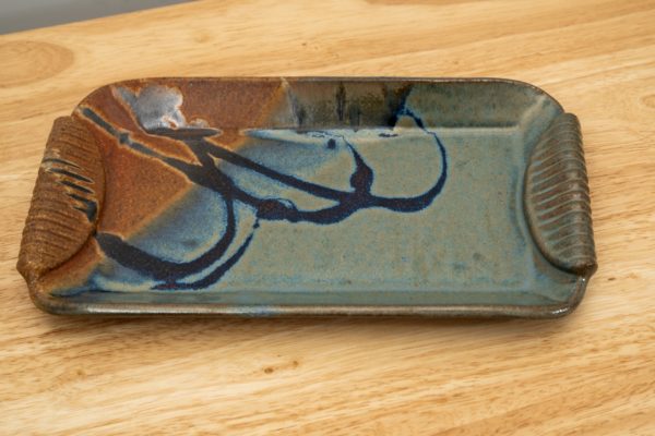 the photograph shows a clay coyote small tray glazed in joes blue resting on a light colored wooden surface. the photograph is well lit with white light.