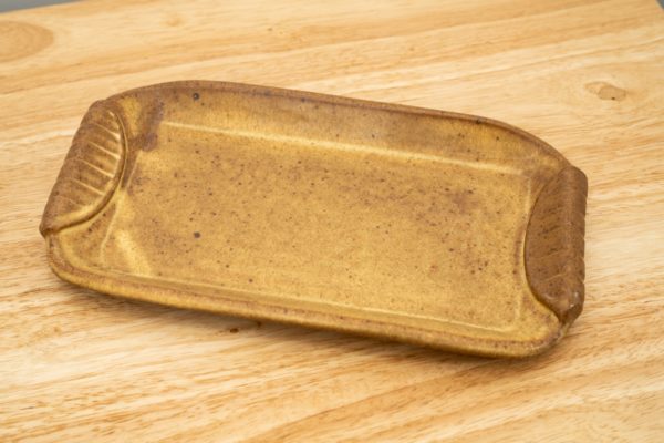 the photograph shows a clay coyote small tray glazed in yellow salt resting on a light colored wooden surface. the photograph is well lit with white light.