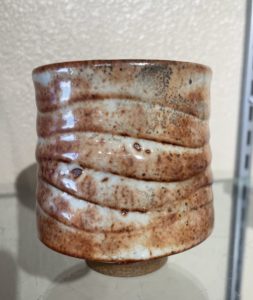 a horizontally framed photograph shows a very close up shot of a clay coyote yunomi glazed in shino. the photograph is so close that the top and bottom of the cup are cut out of the frame. the background is white and out of focus.