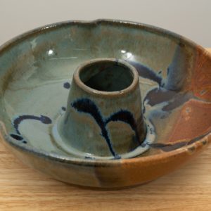 the photograph shows a clay coyote chicken baker glazed in joes blue resting on a light colored wooden surface. the background is a white wall. the photograph is well lit with white light.