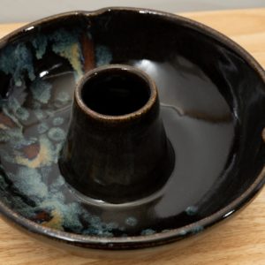 the photograph shows a high angle view of a clay coyote chicken baker glazed in midnight garden resting on a light colored wooden surface. The angle of the the photograph allows the viewer to see inside the chicken baker to see the glaze pattern within. the photograph is well lit with white light.