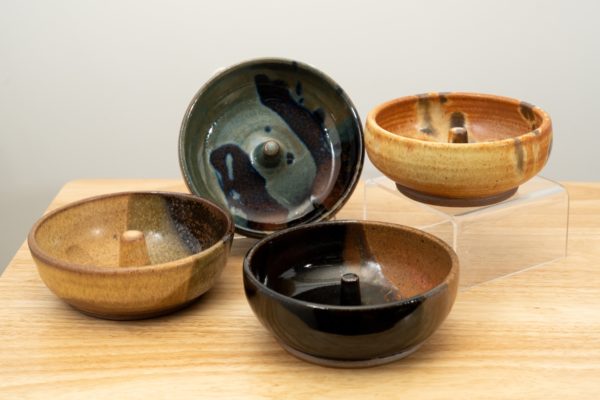 the photograph shows a set of 4 mix-n-match microwave omelette cookers on a small light colored wooden table. starting from the left the glazes on the omelette makers are: tiger, zappa (to the upper right of the tiger) mocha swirl (to the lower right of the tiger) and finally a feather glaze. the zappa glazed omelette cooker is on a plastic stand allowing it to be in a vertical position to show off the glaze pattern. the feather glazed omelette cooker is on a clear plastic riser stand. the background is a white wall.