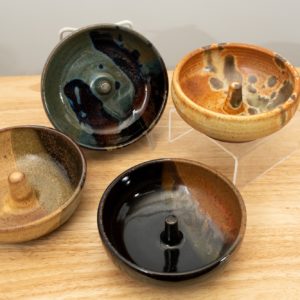 the photograph shows a set of 4 mix-n-match microwave omelette cookers on a small light colored wooden table. starting from the left the glazes on the omelette makers are: tiger, zappa (to the upper right of the tiger) mocha swirl (to the lower right of the tiger) and finally a feather glaze. the zappa glazed omelette cooker is on a plastic stand allowing it to be in a vertical position to show off the glaze pattern. the feather glazed omelette cooker is on a clear plastic riser stand. the background is a white wall.