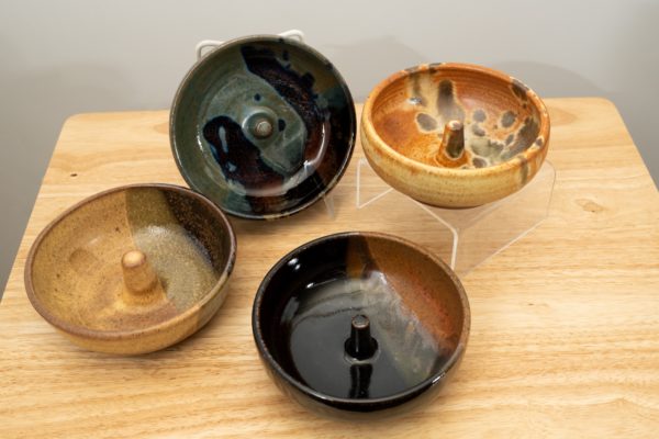 the photograph shows a set of 4 mix-n-match microwave omelette cookers on a small light colored wooden table. starting from the left the glazes on the omelette makers are: tiger, zappa (to the upper right of the tiger) mocha swirl (to the lower right of the tiger) and finally a feather glaze. the zappa glazed omelette cooker is on a plastic stand allowing it to be in a vertical position to show off the glaze pattern. the feather glazed omelette cooker is on a clear plastic riser stand. the background is a white wall.