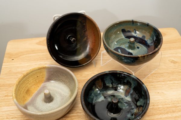 the photograph shows a set of 4 mix-n-match microwave omelette cookers on a small light colored wooden table. starting from the left the glazes on the omelette makers are: mint berry, mocha swirl (to the upper right of the mint berry) midnight garden (to the lower right of the mint berry) and finally a zappa glaze. the mocha swirl omelette cooker is on a plastic stand allowing it to be in a vertical position to show off the glaze pattern. the zappa omelette cooker is on a clear plastic riser stand. the background is a white wall.