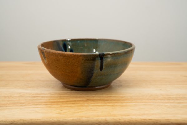 the photograph shows a clay coyote soup and chili bowl glazed in joes blue. the soup and chili bowl is resting on a light colored wooden surface. the photograph is lit with white light.