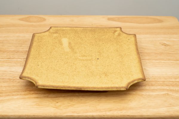 the photograph shows a clay coyote sushi plate glazed in yellow salt resting flat on a small light colored wooden table.