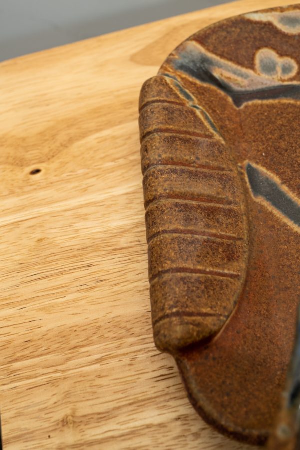 the photograph shows a close up of the handle of a clay coyote small tray's handle. the handle takes up half of the photograph. the tray is resting on a light colored wooden surface.