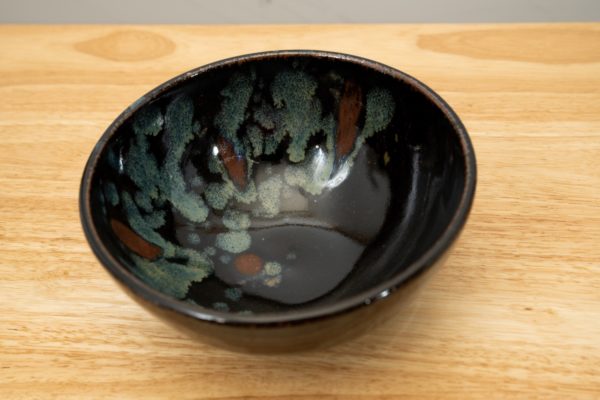 the photograph shows a clay coyote soup and chili bowl glazed in midnight garden resting on a light colored wooden surface. the angle of the photograph allows the viewer to see into the bowl, and see the pattern contained within.