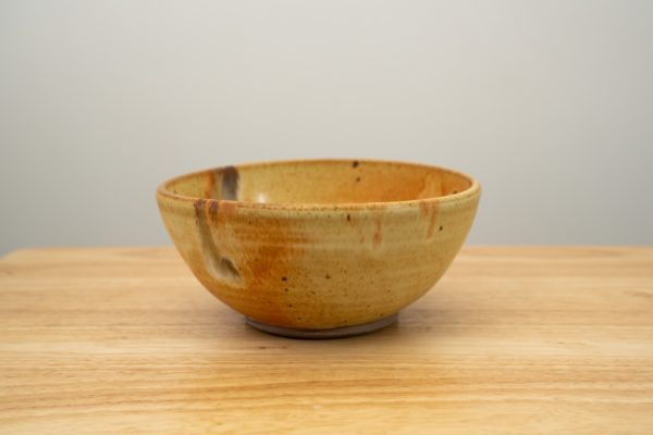 the photograph shows a clay coyote soup and chili bowl glazed in feather resting on a light colored wooden surface in front of a blank white wall. the photograph is well lit with white light. the majority of the feather pattern is in the inside of the bowl, which is not visible in the photograph.