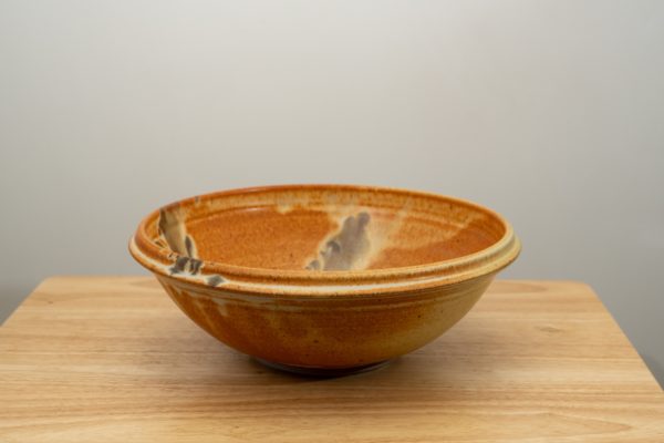 the photograph shows a clay coyote shallow salad bowl glazed in feather resting on a light colored small wooden table. the background is a white wall.