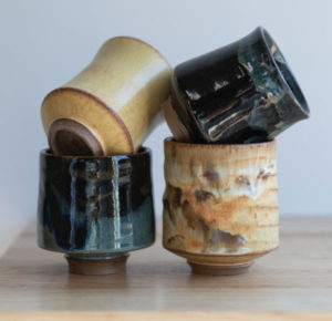 a square shaped photograph shows 4 yunomi wine cups sitting on a table, with a white background. the yunomis are sitting in two stacks of two. the left stack has a yellow salt glazed yunomi resting on top of a zappa glazed yunomi. the right stack has a midnight garden yunomi resting on top of a feather glazed yunomi.