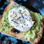 the photograph shows a clay coyote plate with zappa glaze being used to hold a piece of avocado toast, with a poached egg on top. both the avocado and poached egg have everything bagel seasoning sprinkled on them. the photograph is well lit.